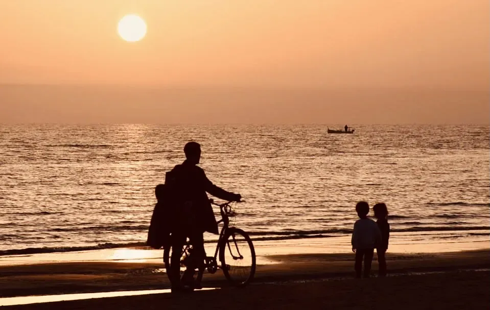 Il tramonto sul mare di Pratoranieri con una famiglia in bicicletta sulla spiaggia