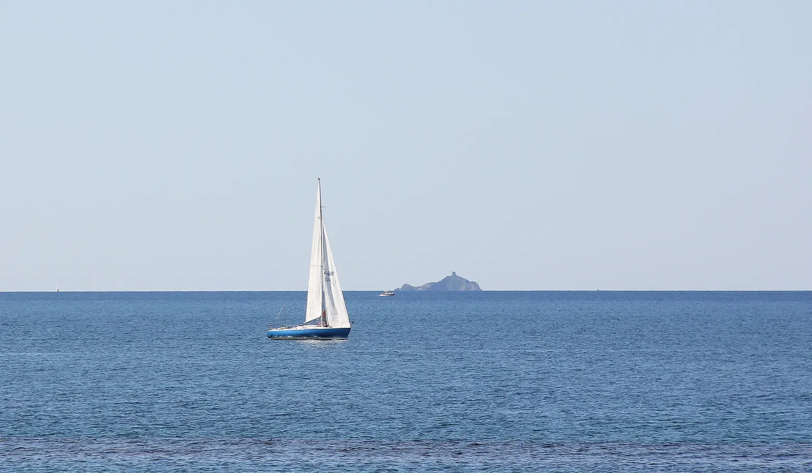 Una barca a vela nel mare davanti a Pratoranieri, con un isolotto all’orizzonte