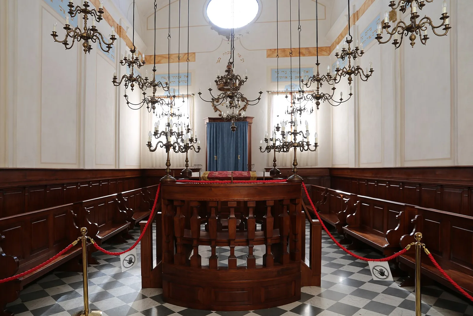 L’interno della sinagoga di Pitigliano con i lampadari, i banchi in legno e l’Aron in fondo